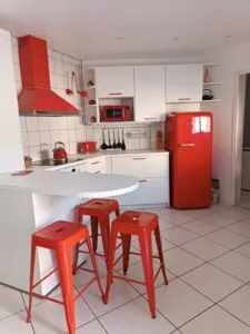Cuisine équipée contemporaine blanche avec îlot central, réfrigérateur rouge et tabourets assortis