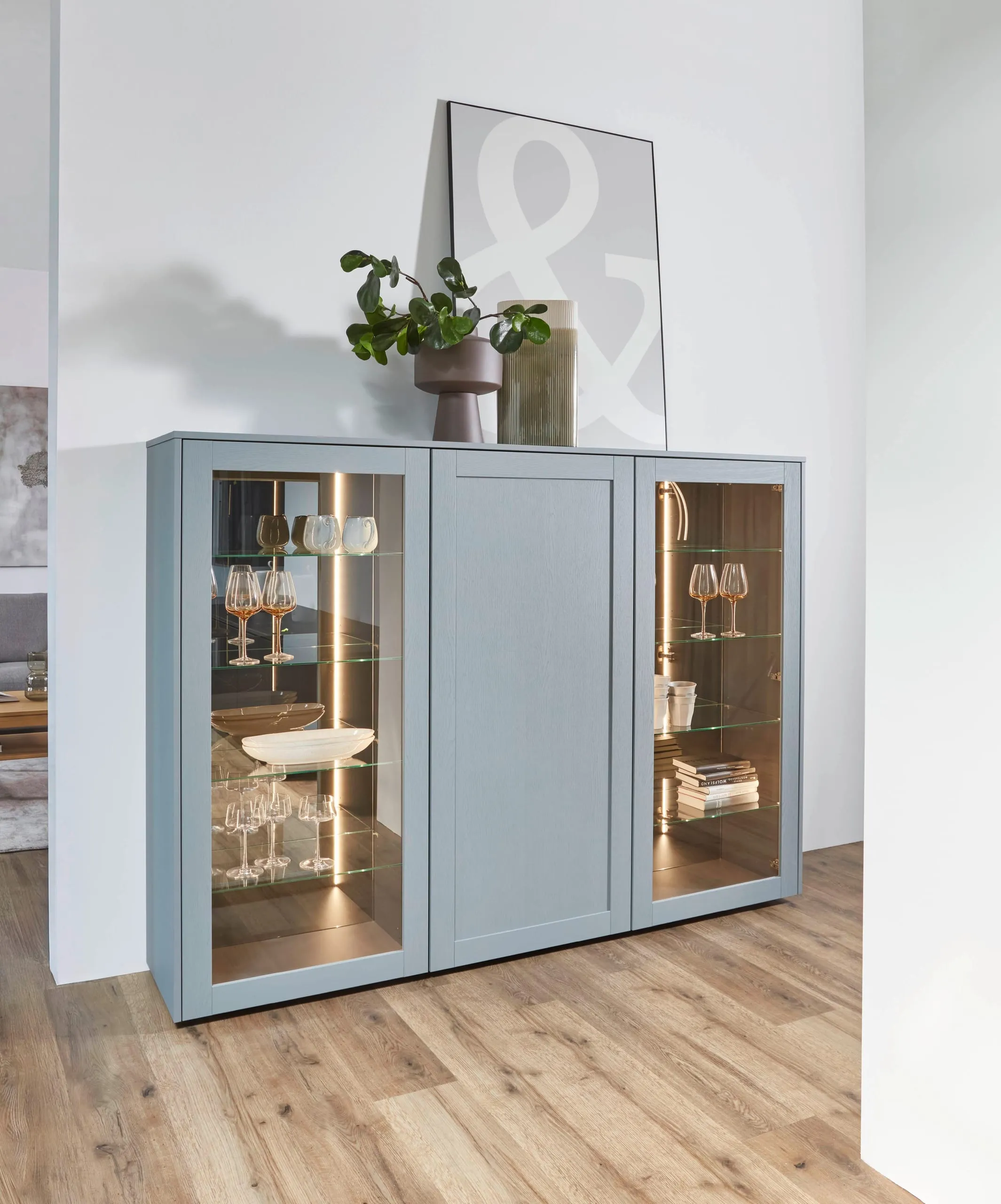 Buffet haut bleu-gris à deux vitrines éclairées, posé sur un parquet clair